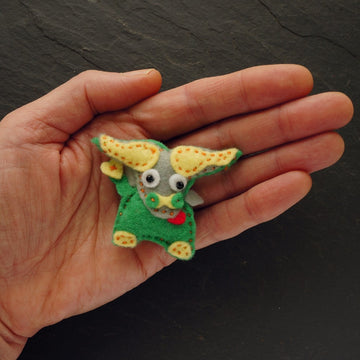 A small handmade felt buffalo in green and yellow, held in the palm of a hand against a dark slate background.