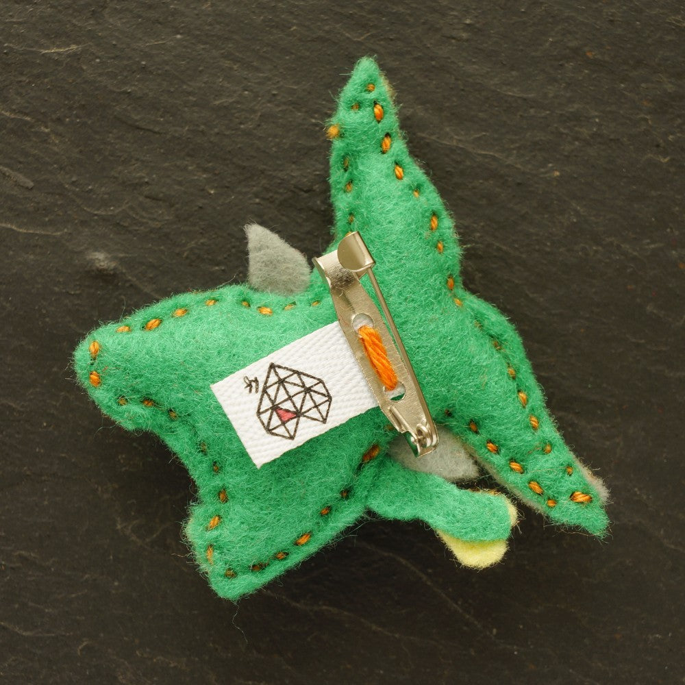 A small handmade felt buffalo in green and yellow, held in the palm of a hand against a dark slate background.