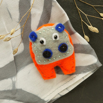 Felt hippo brooch with orange body and blue accents on a fabric background