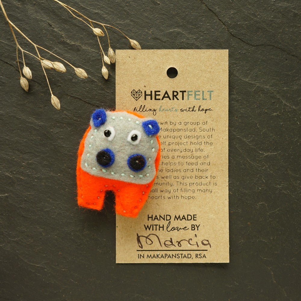 Felt hippo brooch with orange body and blue accents on a fabric background