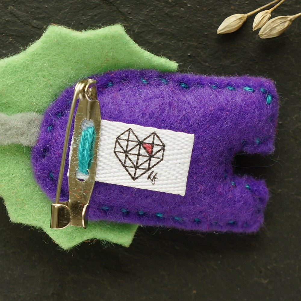 Felt lion brooch with green mane, purple body, cheeky red tongue on spotted purple fabric background