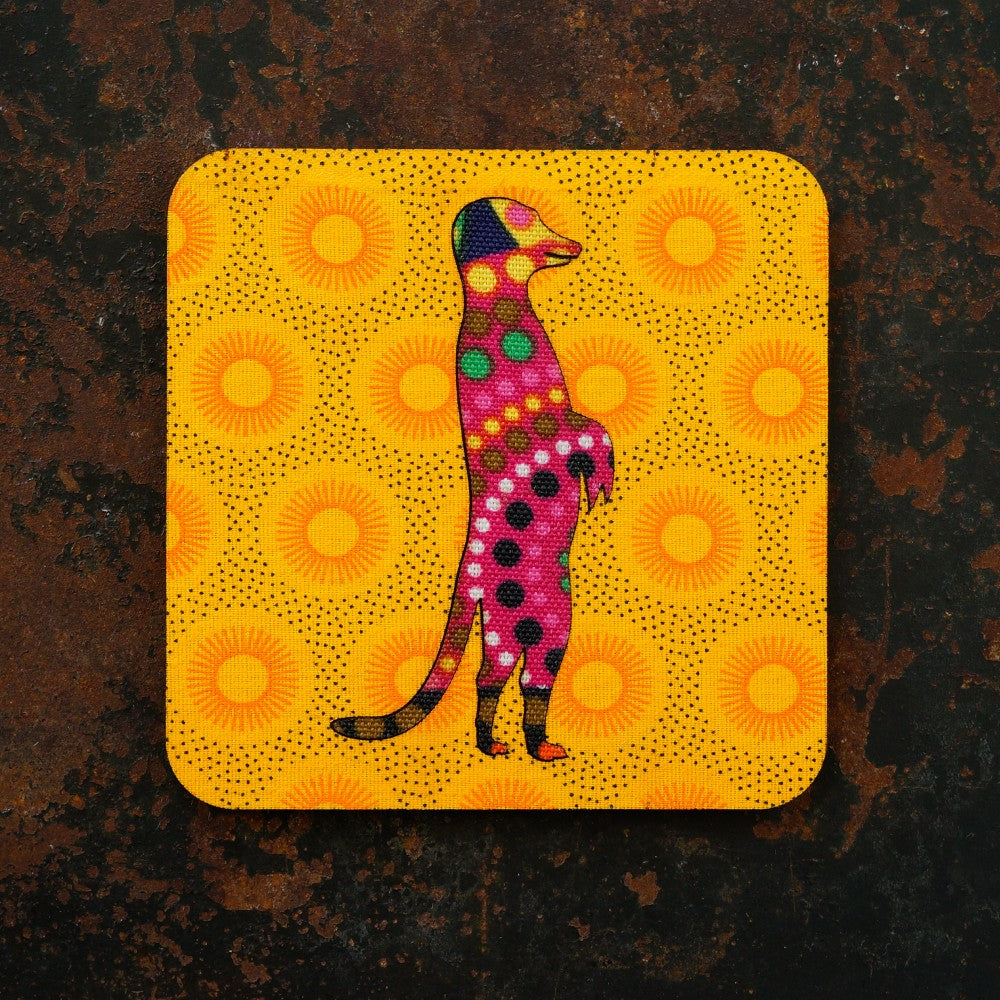 Colourful meerkat illustration on a yellow background with orange sun patterns, placed on a dark brown surface.