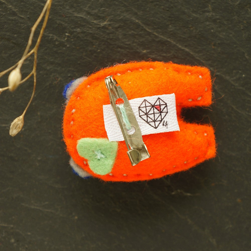 Orange felt hippo backside with a metal pin and heartfelt label on a dark background